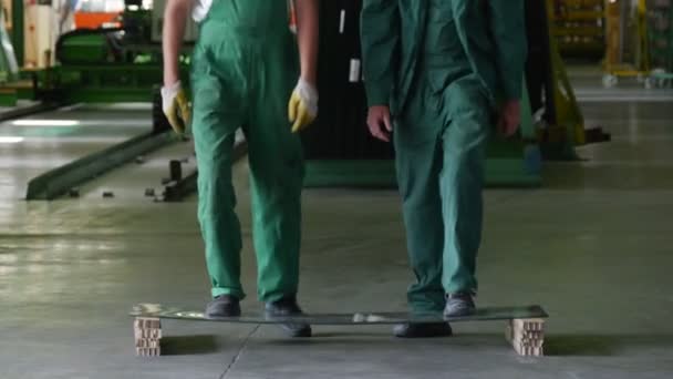 Zwei Arbeiter in grüner Uniform, Stiefel, legen die Glasscheibe auf zwei Blöcke, Männer stehen vor dem Glas, schwanken, prüfen das Glas, Glas ist zerbrochen — Stockvideo