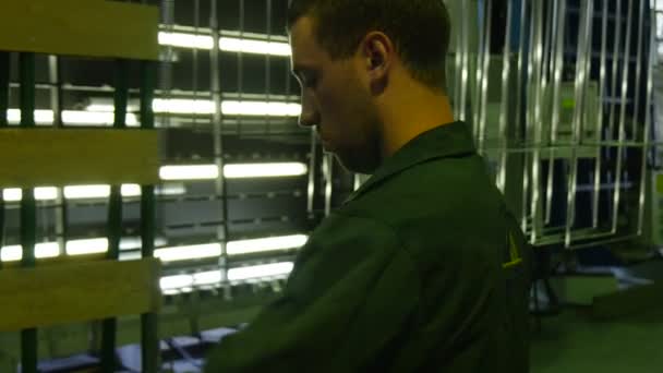 Arbetare i Green Factory Uniform står vid montern med glas, gör metallramar för glasskivor, är Factory Logo på jackan — Stockvideo