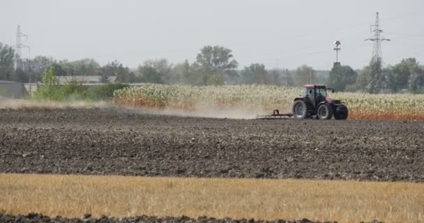 Traktor plowing marken fält växter buskar halm högspännings ledningar torn på en horisont blå himmel — Stockvideo