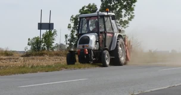 男子驾驶拖拉机与拖车和犁是驱动沿田通过尘土车是路过路树标志尘土飞扬的道路 — 图库视频影像