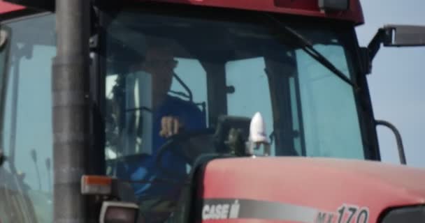 Conductor hombre en tractor está soplando el suelo con árboles de campo de flujo en un tractor Horizonte se acerca Conductor de cerca Hombre en camiseta azul y gafas — Vídeos de Stock