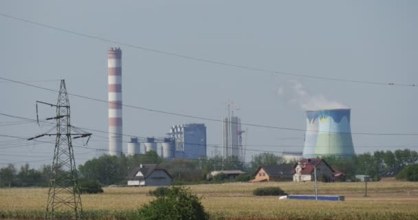 Liggande fält torrt strå hög spänning torn trådar rör av fabriken rök från rör hus på en horisont träd blå himmel — Stockvideo