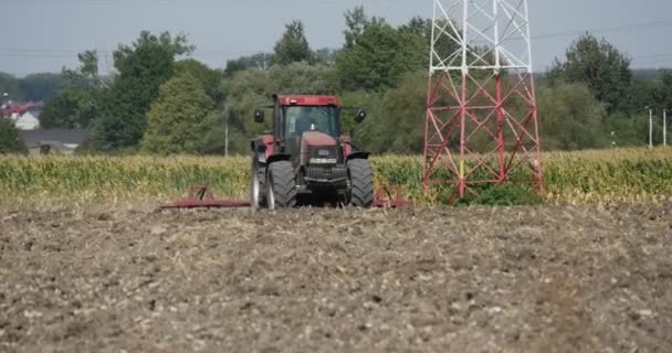 Tractor is Plowing The Field Tracking Right Driver 's Silhouette in Cabin Tractor is Approaching the Camers Trees on a Horizon Street Lamps Road Houses — Vídeo de Stock