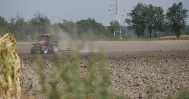 Trattore Distante trattore sta scaricando il campo Polvere volante Le auto stanno passando lungo la strada lungo il campo Torre ad alta tensione rami immagine offuscati — Video Stock