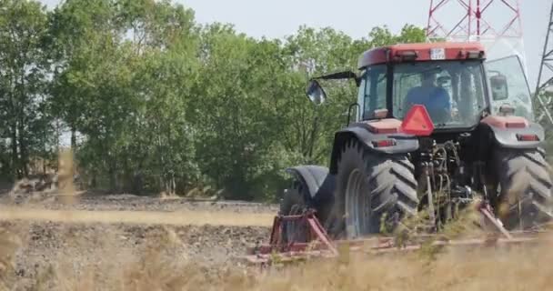 Задній трактор трактора оранка Силуетний знак польового водія на тракторі Високовольтна вежа Зелені дерева Суха трава Вітряний літаючий пил — стокове відео