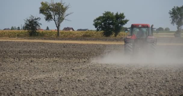 Traktor se distančně pohybuje k levému traktu, kde se rozjede polní cesta podél Fikovaných aut je na silničních stromech podél terénního pole silnice modrá obloha — Stock video