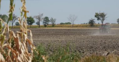 Traktör uzaktan Plowing alan Kara toprak uçan toz arkasında traktör yol boyunca alan otomobil yol ağaçlar Mısır saplarını üzerinde ön plan üzerinde olduğunu