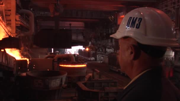 Man werknemer in wit helm met fabriek Logo op helm is op zoek naar oranje licht metaal Metling Man terug fabriek apparatuur — Stockvideo