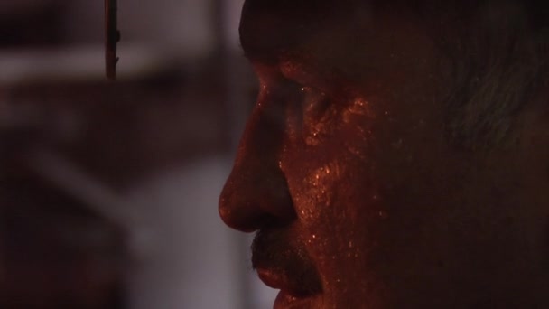 Człowiek z wąsem spocony twarzy oczy Ścieśniać jest patrząc na pomarańczowe światło przez okulary ochronne pracowników mężczyzn w Hełmy ochronne — Wideo stockowe