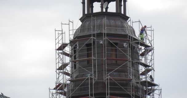 Hombre en ropa de trabajo está montando el andamio alrededor de la torre de la capilla de la iglesia de la catedral gris cielo nublado — Vídeos de Stock