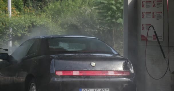 Yong Man lava su cupé de coche deportivo negro en el lavado de autos Close View Wet Asphalt Traffic Cone Green Trees Summer Day Outdoor — Vídeos de Stock