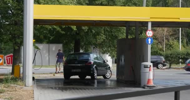 Saubere dunkelgrüne Opel Fließheck fährt weg von der Autowaschanlage Mann steht hinter der Autowaschanlage Autos gehen durch asphaltierte Straße Sommertag im Freien — Stockvideo