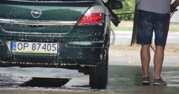 Hombre con cepillo lava cuidadosamente su Opel Hatchback verde en el lavado de autos Limpia ruedas Asfalto húmedo Cerrar Vista — Vídeo de stock