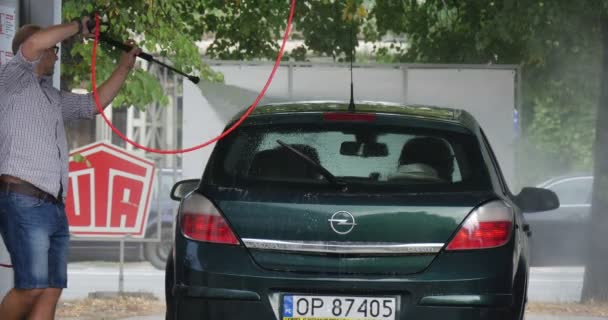 Man in glazen bij de carwash wast zijn groene Opel hatchback aan elke kant groene bomen zomerdag buiten — Stockvideo