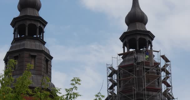 Twee mannen arbeiders op een steiger rond torens twee torens van Kathedraal kerk blauwe hemel wit wolken groene bomen — Stockvideo