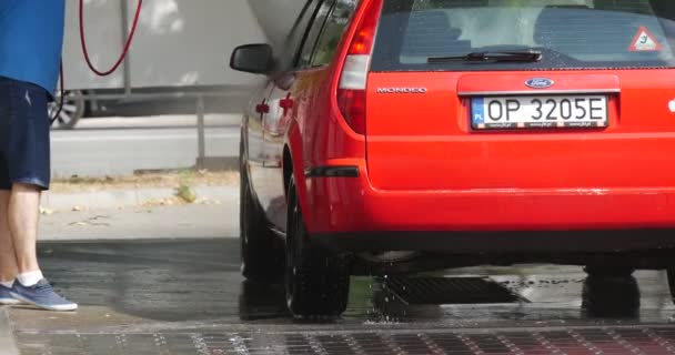 L'homme aux lunettes de soleil lave sa Ford rouge Mondeo à hayon au lave-auto Fermer Voir les arbres verts Journée d'été En plein air — Video