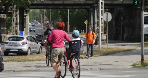 Mężczyźni jeździć na rowerach kobieta z dzieckiem na Baby Seat na rower człowiek z torbą spacery na crosswalk wiele różnych samochodów przejść przez utwardzonej drodze w Opolu Polska — Wideo stockowe