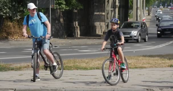 Człowiek i chłopiec w kaski rowerowe jeździć na rowerach dwie starsze kobiety przejść przez drogi różne samochody przejść przez utwardzonej drogi w Opolu Polska letni dzień — Wideo stockowe