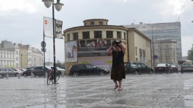 Kadın yağmur yolcu araba binalar lamba mesaj ıslak kaldırım döşeme işaretleri arka plan Bulutlu Sağanak ağır çekimde yürür