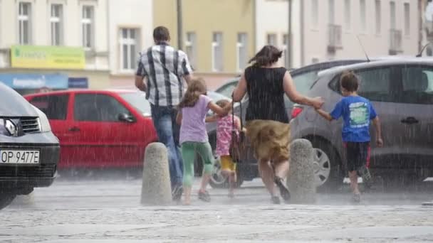 Férfi és nő, három gyerek futtassa az eső, esernyők nedves úton épületek autók zápor nyári nap nélkül Opolskie Lengyelország vissza nézetben-lassított — Stock videók