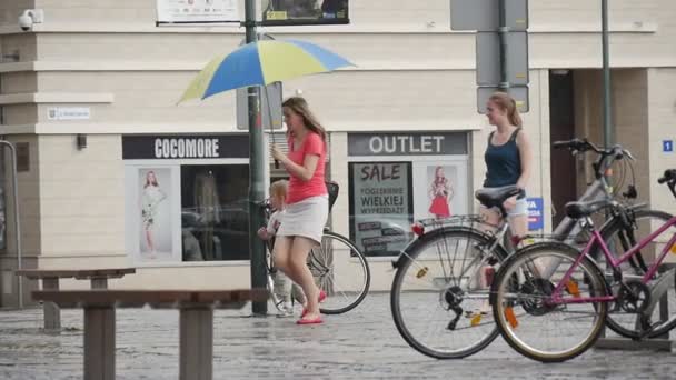 Mujer con niño corre bajo la lluvia bajo paraguas amarillo-azul Otras dos mujeres caminan bajo la lluvia sin paraguas aguacero en Opole Polonia cámara lenta — Vídeos de Stock