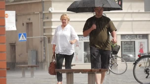 Oudere vrouw en Man met paraplu lopen in de regen gebouw geparkeerd fietsen banken verkeer borden Slow Motion nauwe weergave — Stockvideo