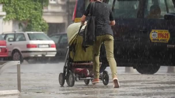 Молода жінка з Baby Прам працює під дощем без парасольки поблизу стояти припаркованих велосипедів і автомобілів злива в Ополе Польщі Близький вид повільний рух — стокове відео