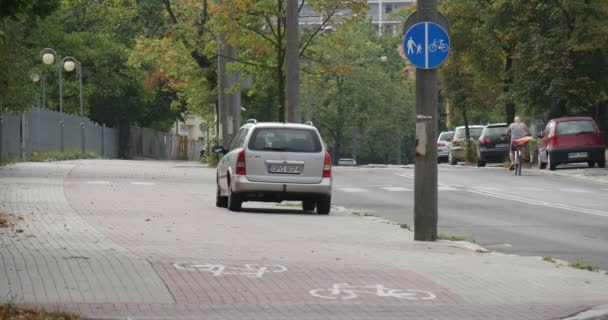 Припаркованные автомобили Человек на велосипеде проходит по автомобильной дороге синий серебристый темно-зеленый автомобили идут по асфальтированной дороге Боковая Зеленые деревья летом осенью в городе — стоковое видео