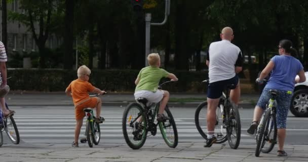 Két fiú-férfi és nő a kerékpárok odalép a Crosswalk majd lovagolni, egész Crosswalk autó megáll a közlekedési lámpák napsütéses nyári napon utca-és városrészlet — Stock videók