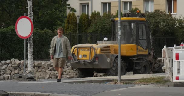 Genç adam sarı buldozer yol onarım trafik işareti kırmızı-beyaz barikat yaz günü açık Opole Polonya Görünümü Kapat yakınındaki kaldırımda yürüyor — Stok video