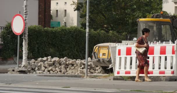 El çantası ve kırmızı plastik torba kadın ile asfalt yol onarım işleri kırmızı-beyaz barikat sarı buldozer trafik işareti gün açık Opole Polonya üzerinde yürüyor — Stok video