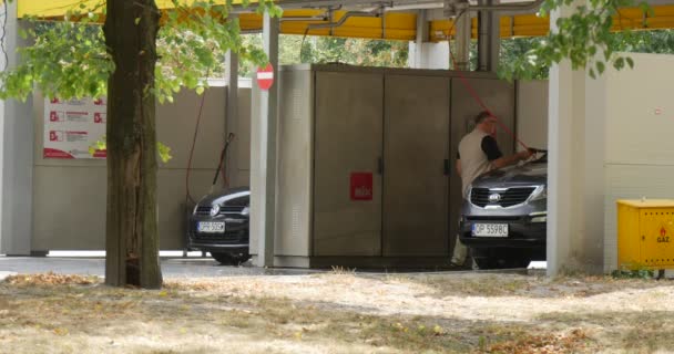 Człowiek z wiadra w jego ręce myje srebrny samochodu na myjni ciemny niebieski samochód stoi w innym polu Carwash lato dzień Opole Polska — Wideo stockowe