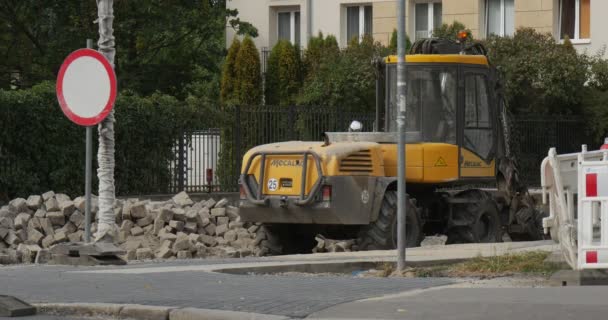 L'uomo cammina sul marciapiede giallo Bulldozer Red Station Wagon va da strada asfaltata lavori di riparazione dei materiali da costruzione Segnale stradale alberi verdi e cespugli — Video Stock