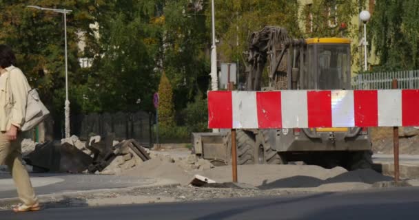 Dvě ženy chodit na asfaltovou silnici buldozer stojí na chodníku zátaras stavební materiály lampa příspěvky bílým plotem zelené stromy den Opole Polsko — Stock video