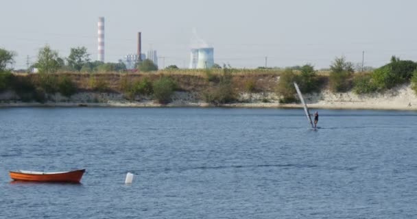 Windsurfer Man sta galleggiando sul lago Barca vuota sui tubi della fabbrica dell'acqua su un fumo Horizon da tubi Le auto stanno passando dalla strada dietro il lago — Video Stock