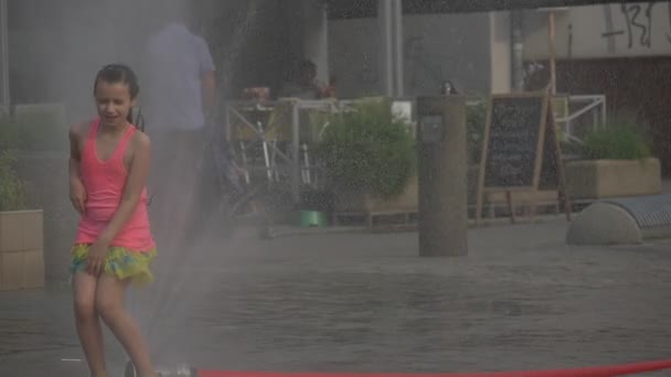 Підлітка дівчина в рожева Маєчка купання у The Spray води fountain, який був створений пошкоджених пожежного Рукава — стокове відео