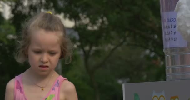 Una niña pequeña ha saltado sobre una pierna y que obtiene un algodón de azúcar de la mano de un vendedor — Vídeo de stock