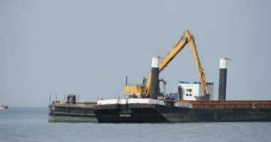 Sarı mavna Aggradation Barajı Groynes bina işleri deniz yaz günü açık Bkue gökyüzü martılar deniz manzarası, toprak yaratılması Ekskavatör üzerinde
