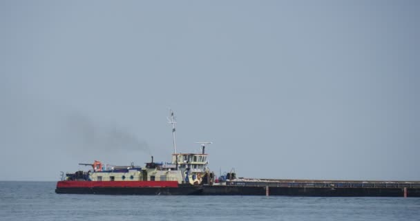 Lungo nero carico chiatta galleggia sul mare anziana donna cammina sulla riva creazione di dighe roynes costruzione funziona al mare estate giorno cielo blu paesaggio marino — Video Stock