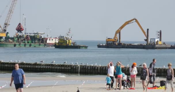 Gezin met kinderen op de kust mensen lopen op het zandbak met kraan en Barge met graafwerk op de zee Aggradation van de bodem creatie van Dam Groynes — Stockvideo
