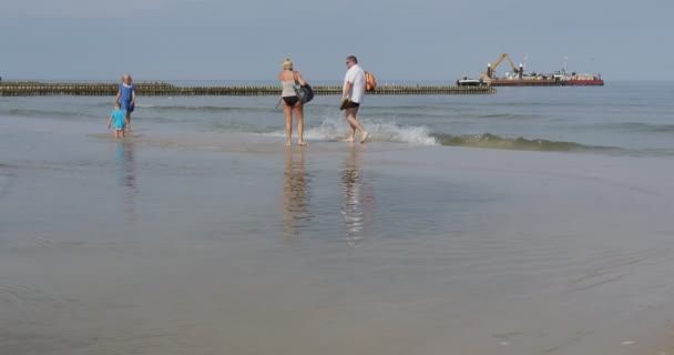 Människor går på stranden barnen leka i vattnet två pråmar arbete vid havet Aggradation av marken skapandet av dammen groynes byggnad arbetar vid havet Leba Polen — Stockvideo