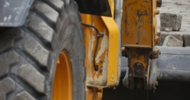 Workers Man in Orange Workwear is Working Loading the Stones to the Scoop Yellow Excavator Close Up Wheels Close Up Road Repair Blocks Outdoors Sity