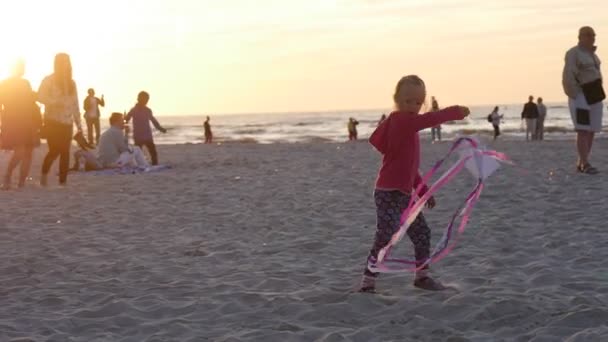 Menina voa a menina pequena pipa está balançando pessoas famílias silhuetas estão andando na praia crianças estão jogando internacional pipa Festival Leba Polônia — Vídeo de Stock