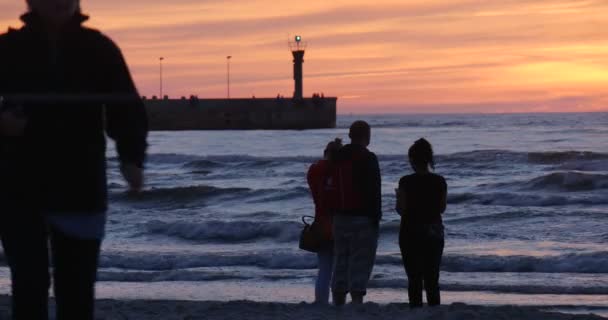 파도 부두 일몰 저녁 야외 핑크 노란색 하늘을 찾고 해변 해안선에 바다에 서있는 사람들 커플 의 그룹 — 비디오