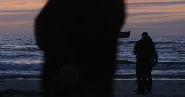 Pareja hombre y mujer están de pie en el mar caminando gente costa costa mar moviendo barco sobre fondo rosa cielo olas nubes noche puesta del sol al aire libre — Vídeos de Stock