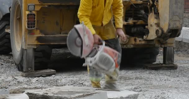 Hombre trabajador en ropa de trabajo amarilla comienza a moler los bloques de hormigón mediante la rectificadora Close Up Yellow Excavator Flying Dust Road Repair — Vídeos de Stock