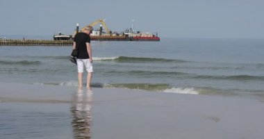 Elinde Ayakkabı ile Man Deniz Kıyısında Yalınayak Walks Ve Denizde Mesafe İnşaat Mavna Su Denizi Surf Breakwater Yılında Ayaklarını Islak