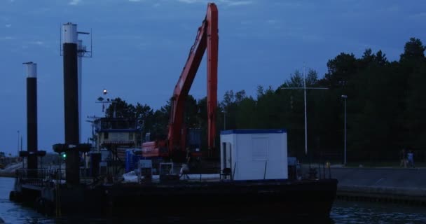 Bouw schip met graafmachine op het bord zwemt in de haven schip Tows een boot achter het schip zwemt zeilboot silhouetten in de donkere schemering — Stockvideo