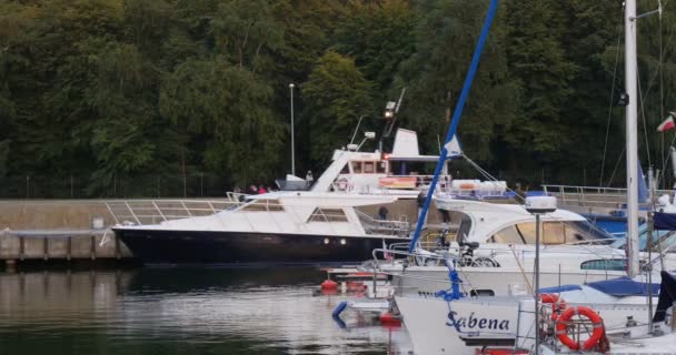 Barco branco com pessoas na placa nada para fora do porto As pessoas caminham em iates quay são colocados Yacht Club Port Calm Clear Water Cloudy Weather Sunset — Vídeo de Stock