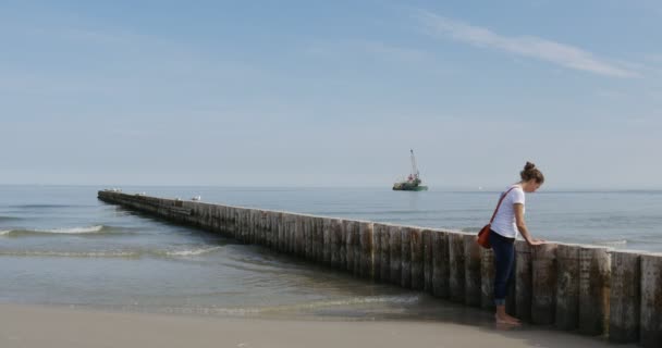 Lonely Girl Barefoot Stands On The Sand Loneliness Sadness Dreaming Girl Breakwater Sea Surf Small Waves Tide Sandy Sea Shore Sunny Summer Day — Stok Video